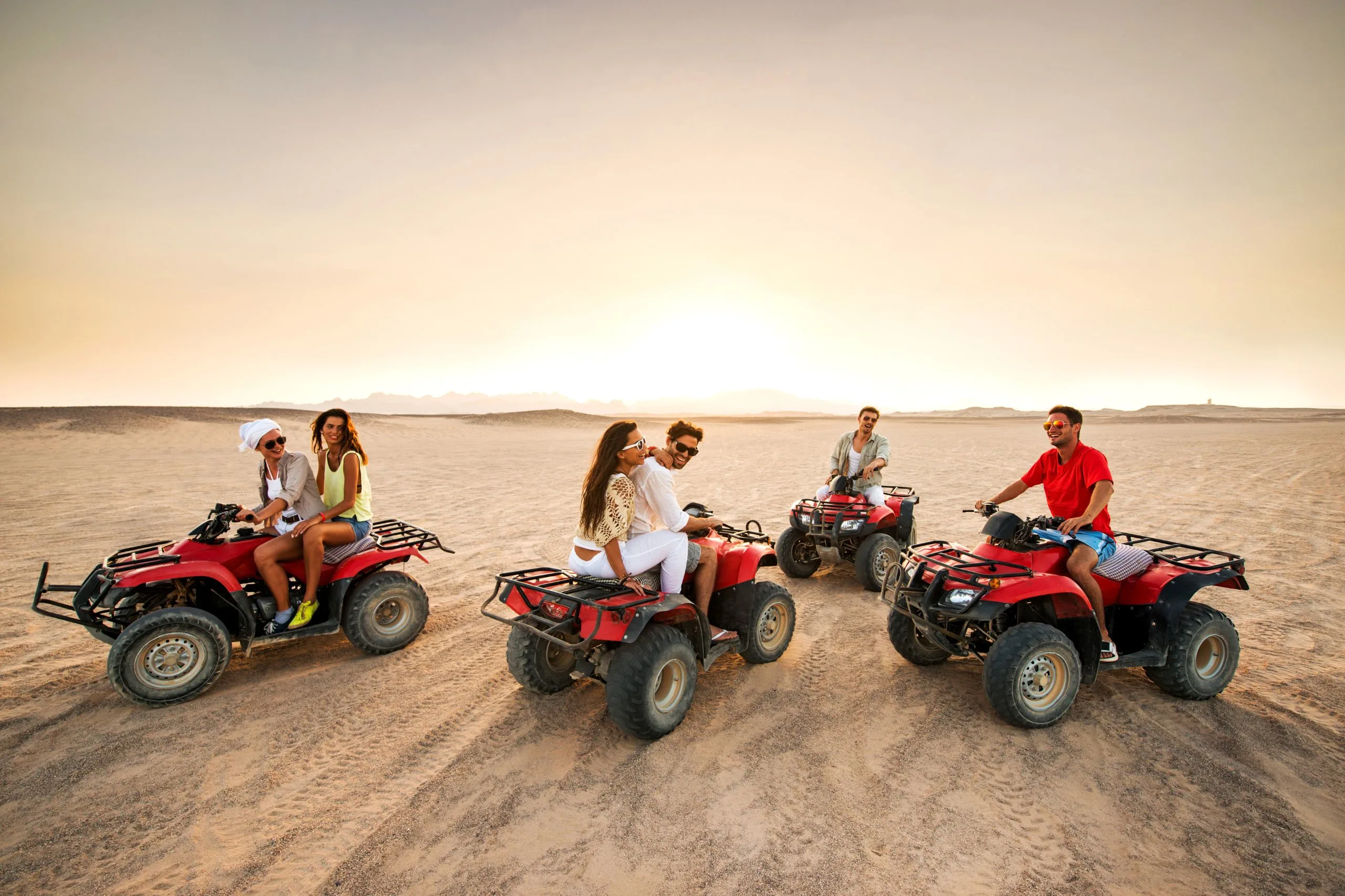 Group of friends riding red ATVs in a desert at sunset.