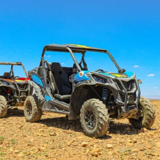 Two all-terrain UTV buggies parked on rocky desert terrain under a clear blue sky, ready for an off-road adventure.