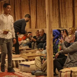 People enjoying traditional Moroccan tea in a rustic tea house with low seating, rugs, and local servers.