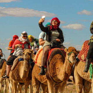 Group of tourists riding camels in the scenic Agafay Desert near Marrakech under the clear blue sky.