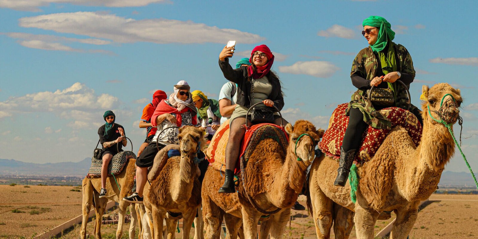 Group of tourists riding camels in the scenic Agafay Desert near Marrakech under the clear blue sky.