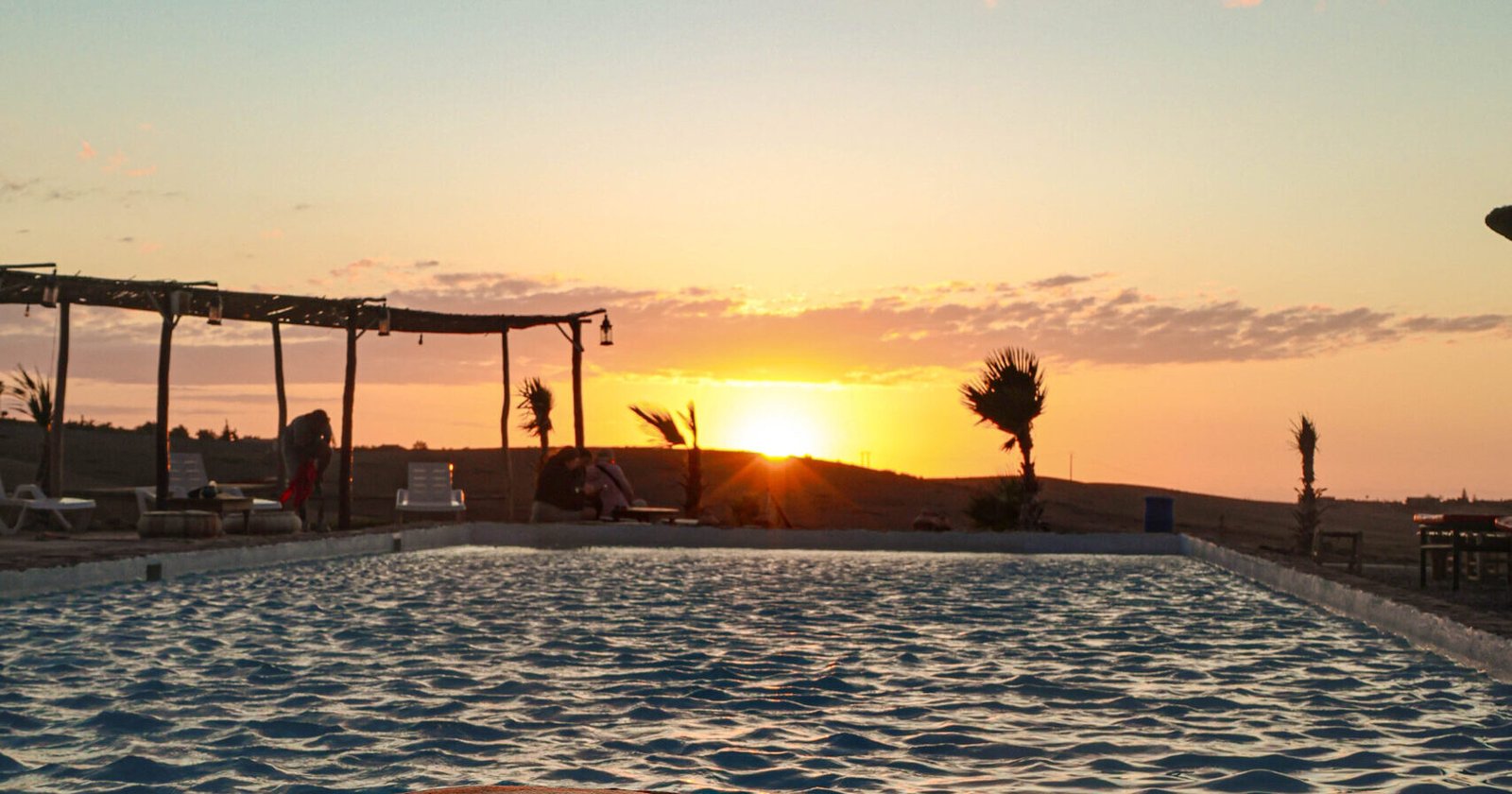 Luxuryairs desert resort poolside at sunset with elegant seating, palm trees, and tranquil ambiance.