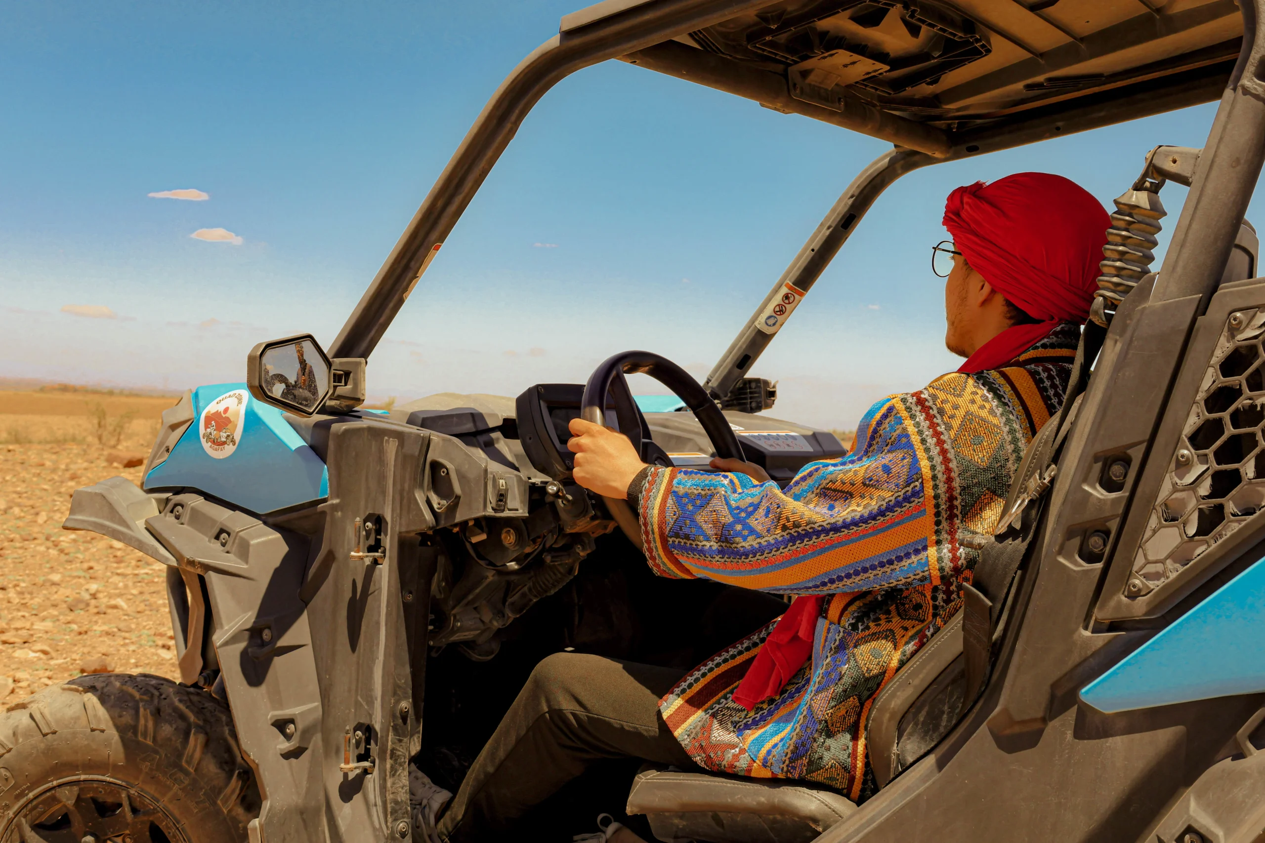 Man in traditional Moroccan attire driving a buggy through the Agafay Desert under a clear blue sky
